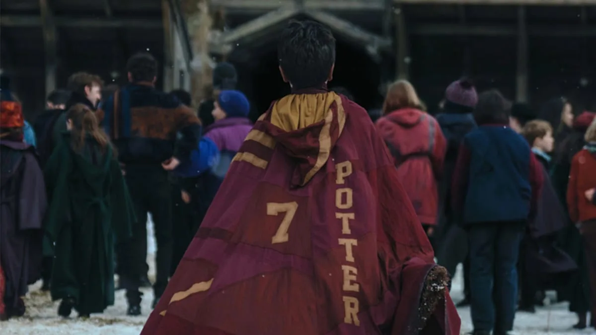 A student in a red and gold robe with Potter and the number 7 on the back, walking through the snow in HBO's Harry Potter series